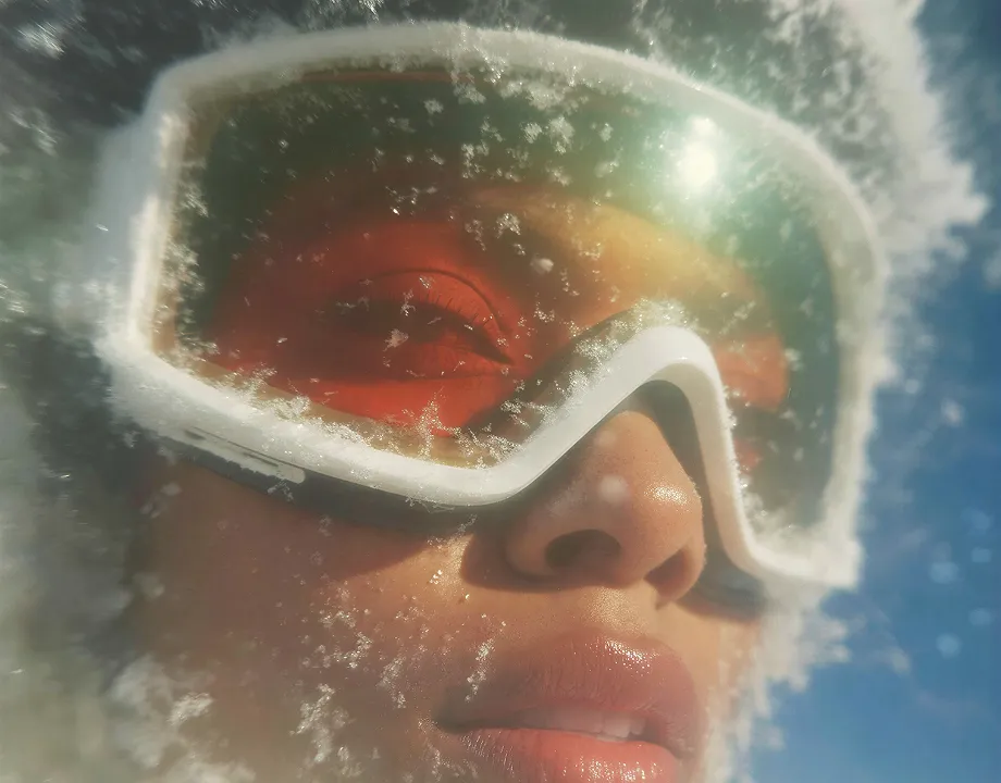 Close-up of a person wearing frosted ski goggles with snow and ice on the lenses and face.